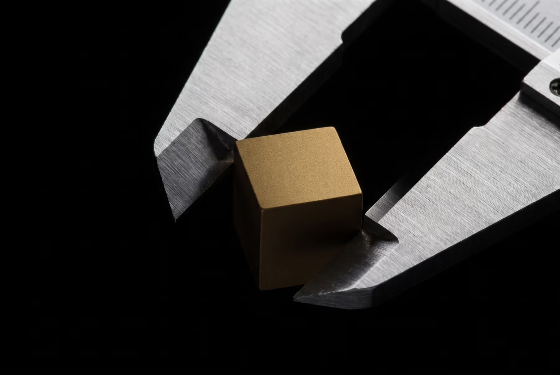 Precision caliper measuring a gold cube against dark metal